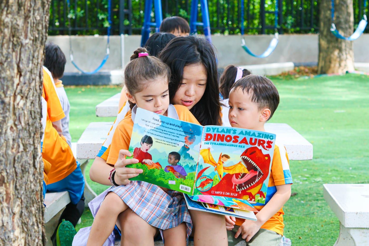 Early Years children sharing a picture book on the grass at BCIS
